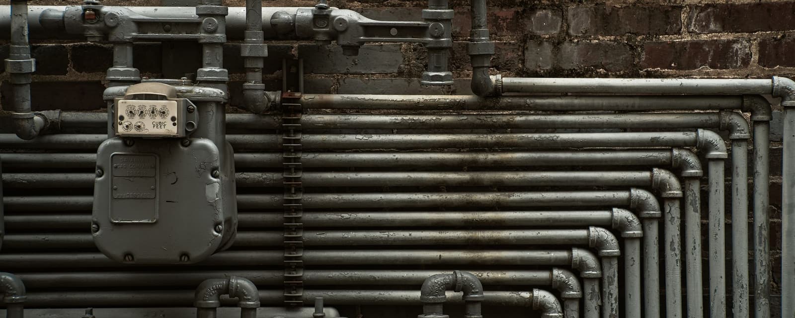 Steel pipework running along a brick basement wall.