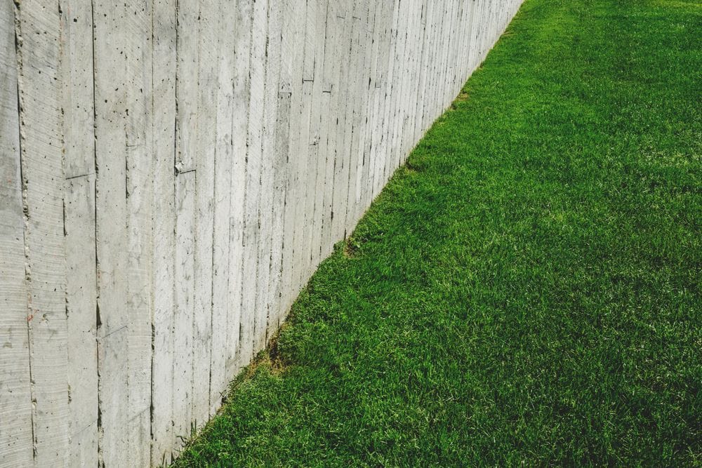 A wooden fence running alongside a green lawn.