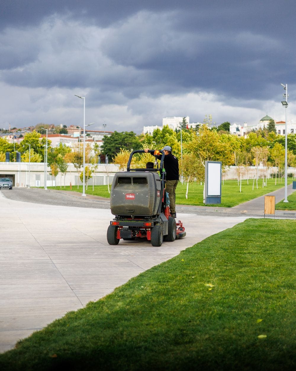 A ride-on mower cutting a wide lawn under a cloudy sky.